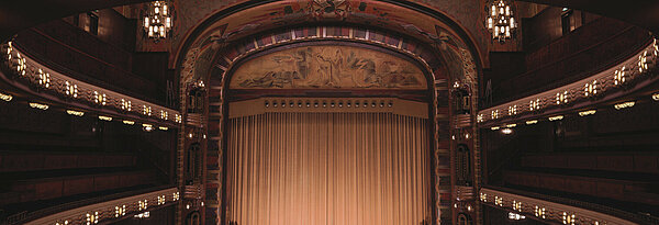 Bühne mit Vorhang und Ränge in dunkelbeleuchtetem Theater mit Kulturprogramm